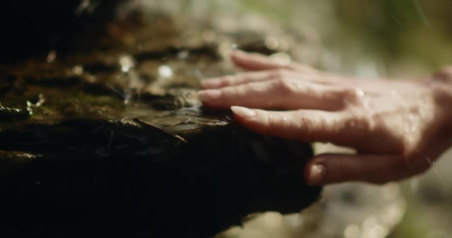 A person touching rocks that have water flowing over them