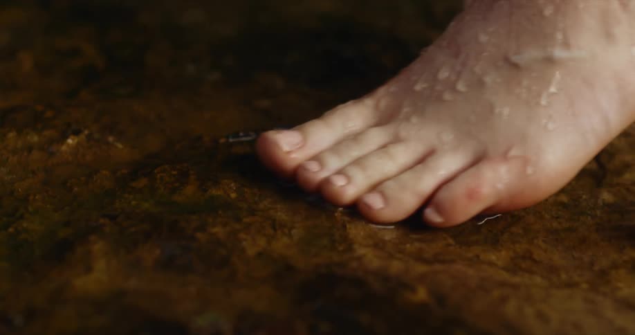 A person carefully and slowly moves their feet as they step in a shallow stream of water