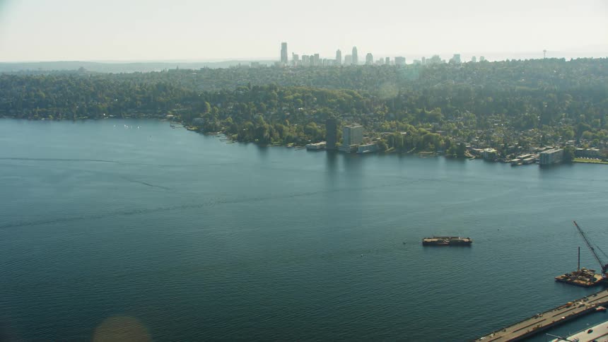 Cars travel across a highway bridge with a coastal city and skyline on the horizon