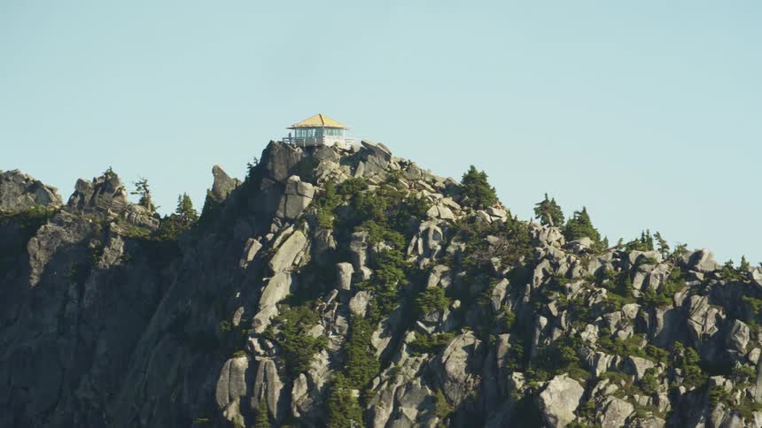 A small building on the peak of a narrow mountain ridge under a clear daytime sky
