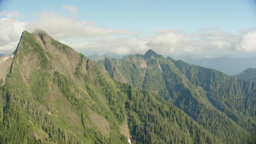 A tall and rocky mountain range is covered in vibrant green forests
