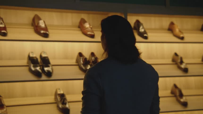 Man stands looking over display of leather shoes sitting on wooden shelves