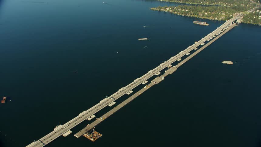 A bridge with vehicles over a river with land and houses in the background