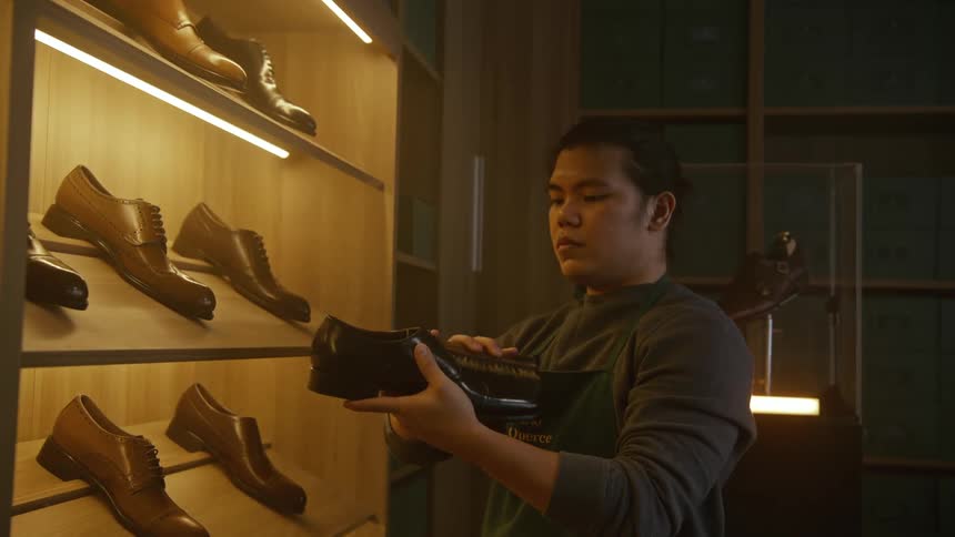 A man with a apron in a shoe store shining a shoe with a brush