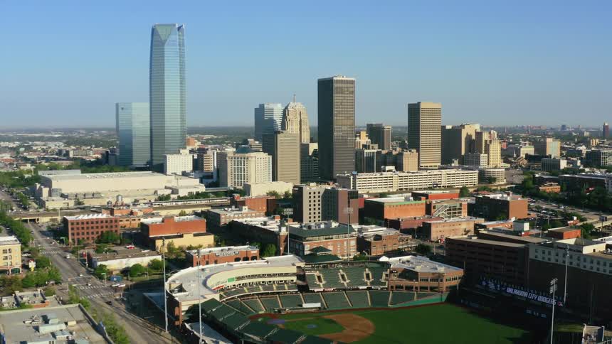 A baseball stadium and several skyscrapers are located within a metropolitan area