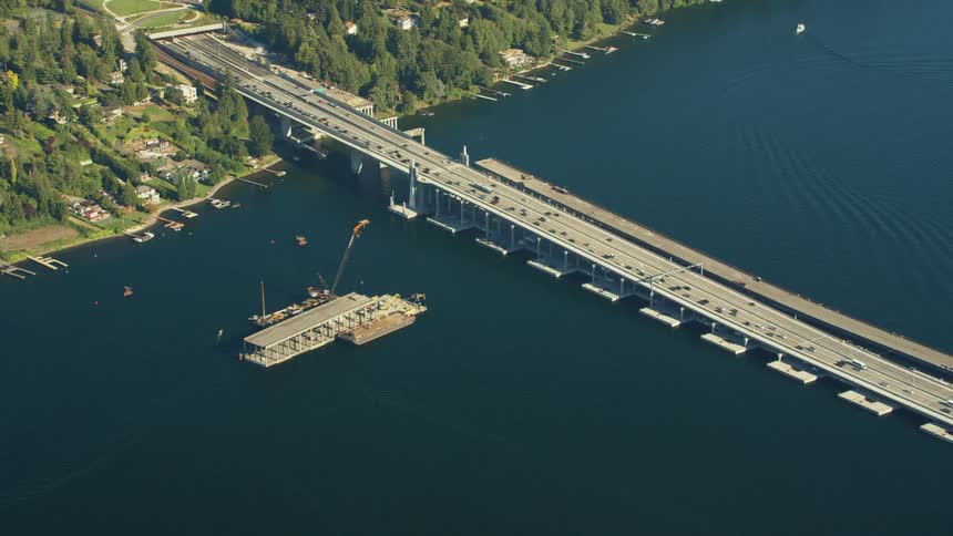 Traffic flows across bridge near floating dock to and from tree covered town