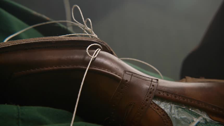 A shoemaker attaches a sole to a leather leather with thick thread