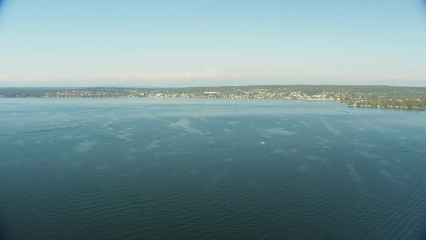 Boats travel in the ocean near shore leaving wakes in the rippling surface