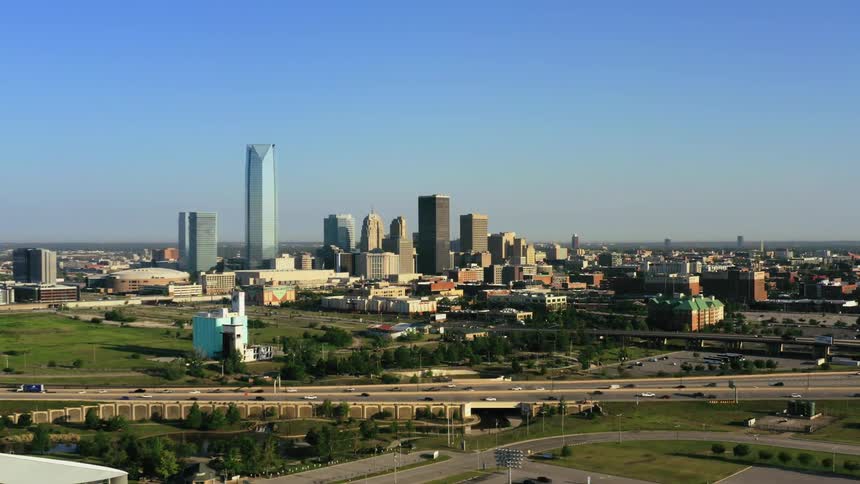 Traffic travels along a highway as skyscrapers loom in the background on a clear day