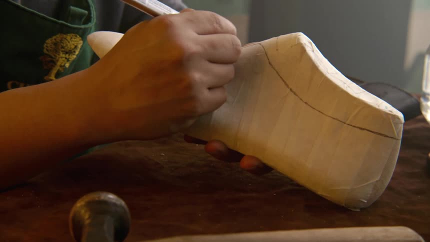 A shoe maker uses a pen to outline a shape on a shoe block