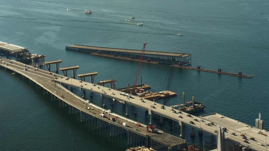A bridge with vehicles over a river with boats and land in the background