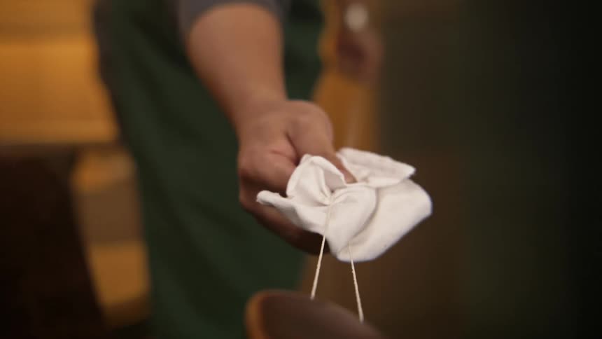 A man holds two strings taut as he wipes the length of them with a white cloth