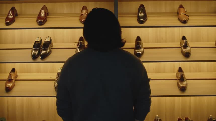 A man stands before illuminated shelves holding leather shoes