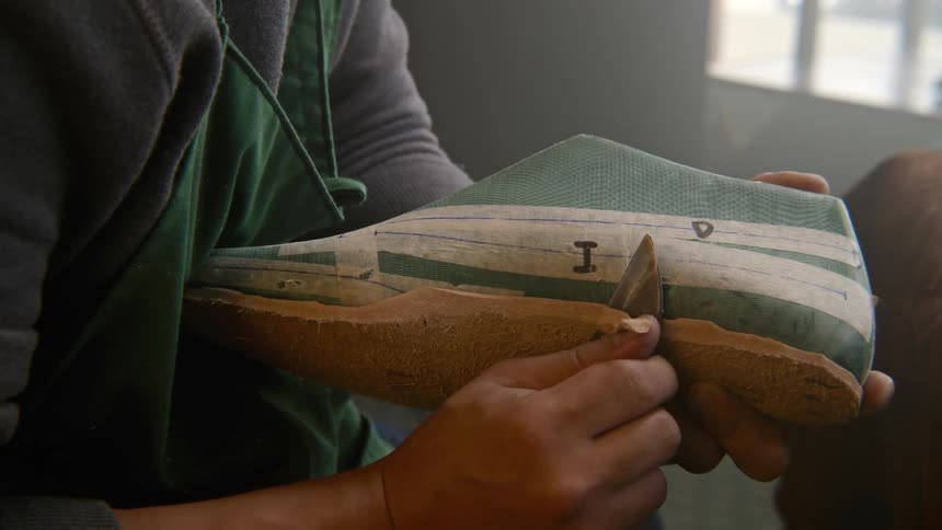 A man trims the sole on a shoe as he makes it