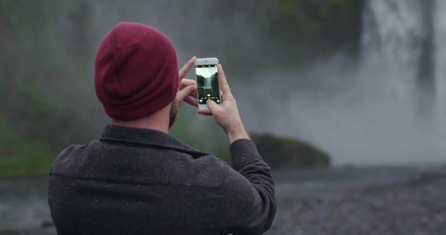 A man photographing a waterfall with his cell phone