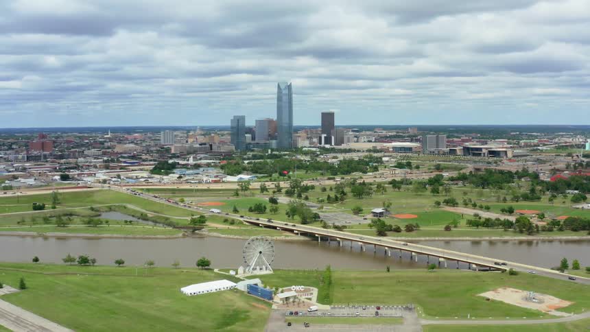 A city with buildings trees and a bridge with the sky and clouds in the background