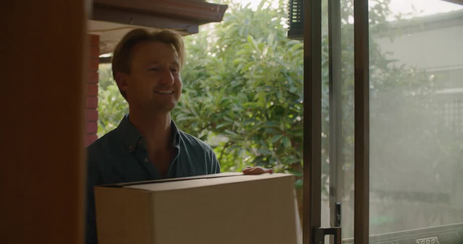 A woman and man carry boxes into a building while talking with one another
