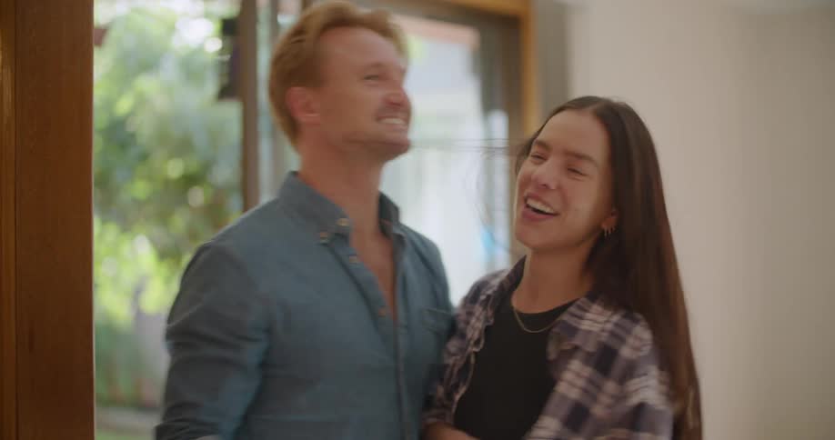 Man and woman smile and hug before talking while standing just inside door showing lawn