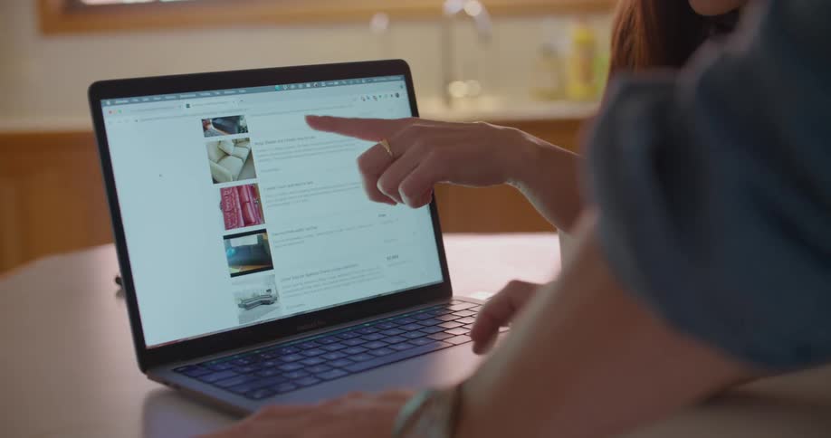 Two people lean over counter in kitchen shopping on laptop