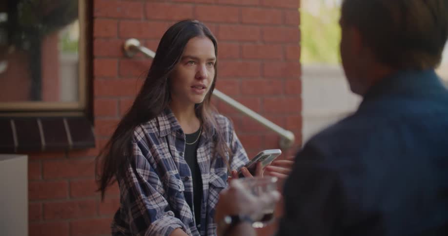 A young woman holds a smart phone while sitting an talking to a male companion
