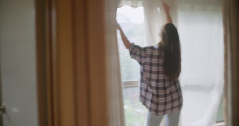 A man slides a washing machine in to place as a woman hangs drapes in a house