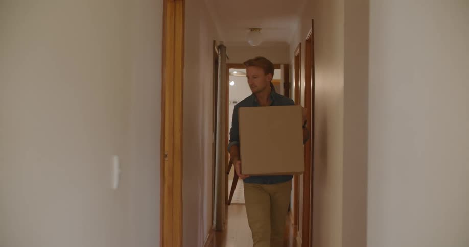 A man and a woman walking down a hallway with the man carrying a box and the woman carrying a chair