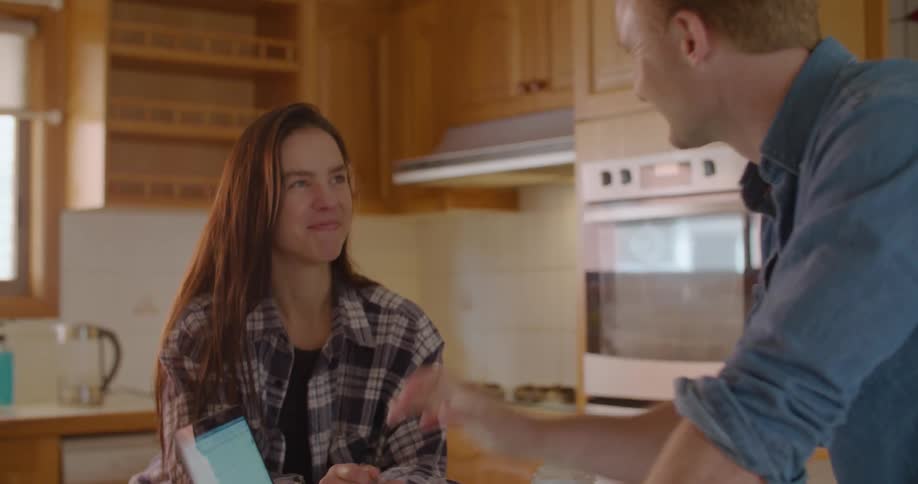 A woman in a kitchen holds a credit card as a man uses a laptop and then they both high five one another