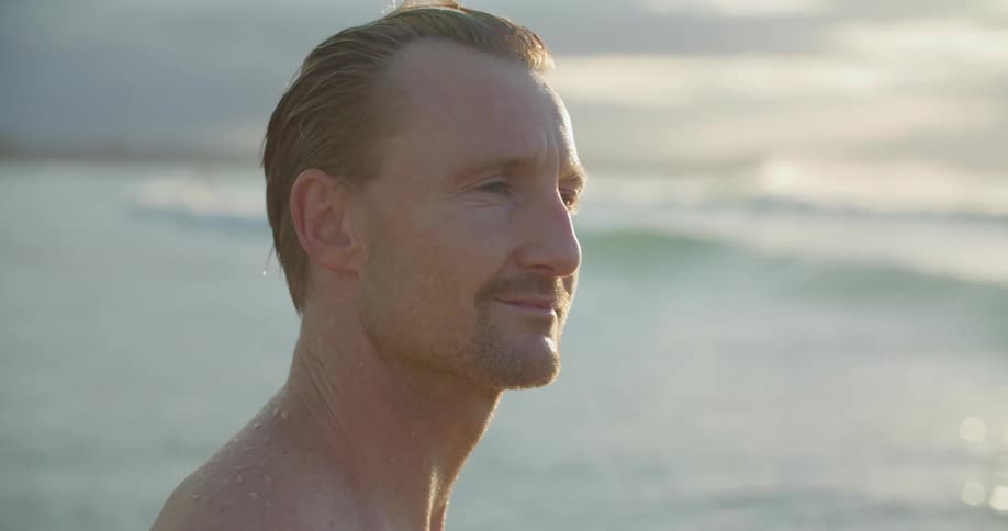 Wet man stands and looks around on the beach smiling