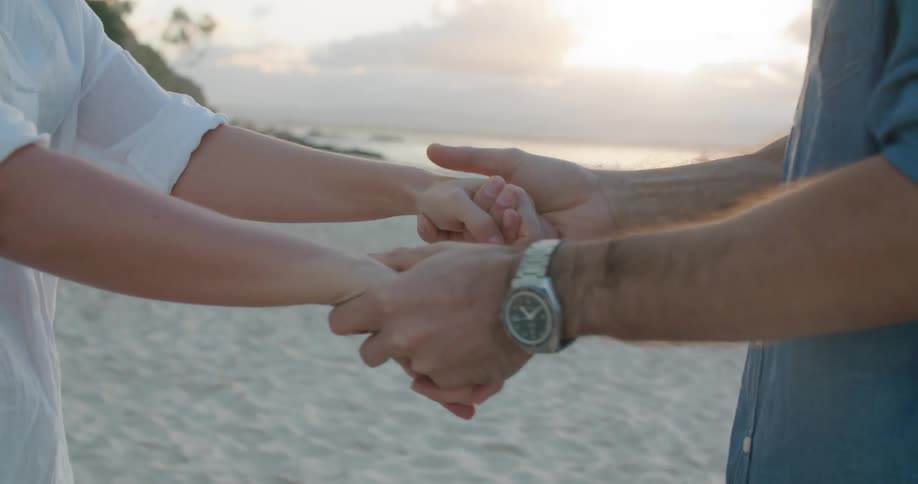 A man and woman hold holds while facing each other as they stand on a sandy beach