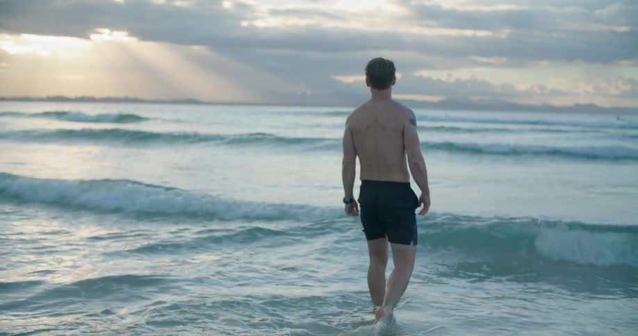 A man is wearing swimming trunks at beach and walking into the sea