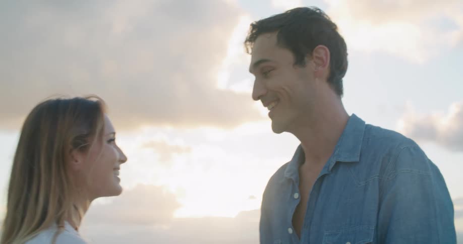 Husband and wife are kissing at the beach while the sun sets