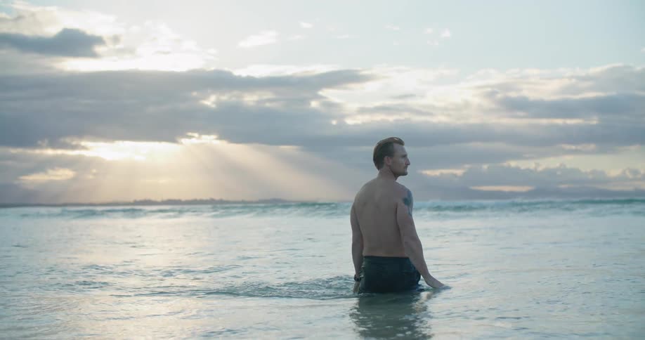 A man stands in waist high water in the ocean