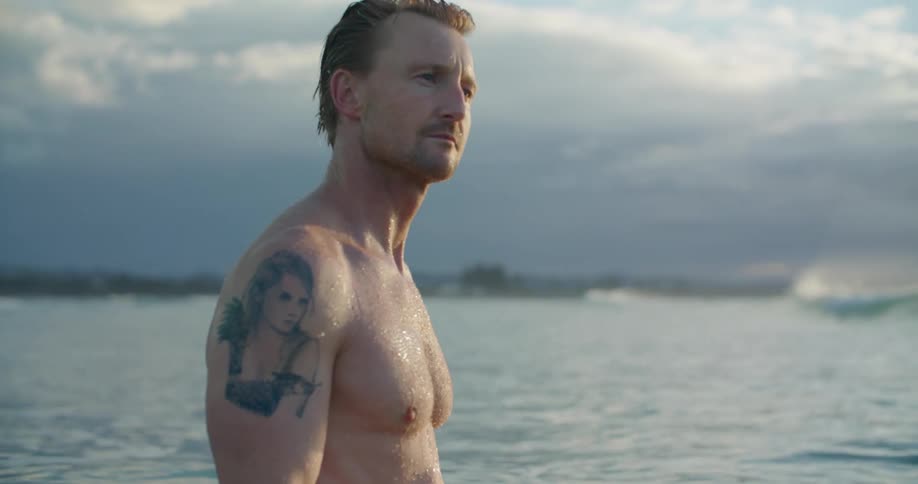 Man smiles standing in ocean as waves roll across surface under clouds