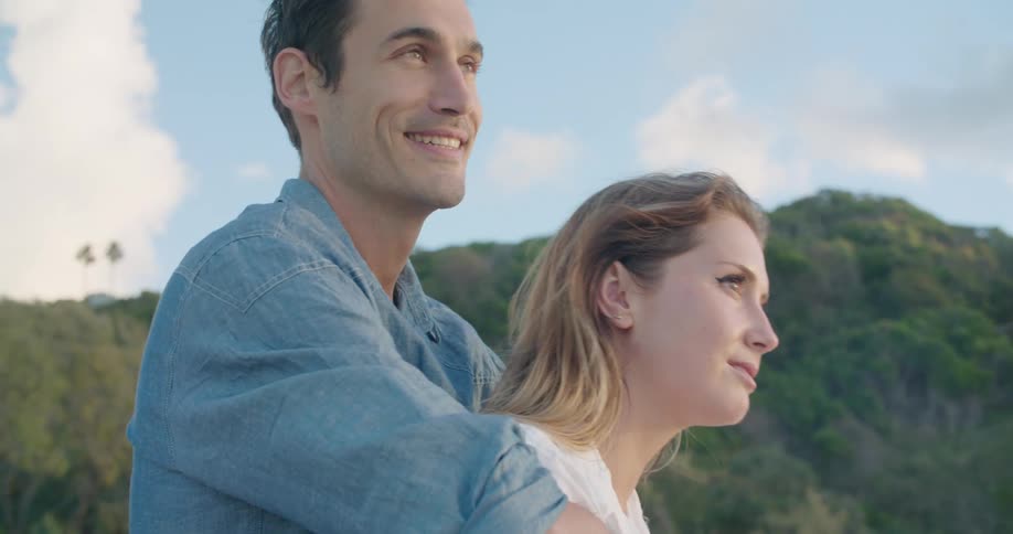 A man stands behind a woman and hugs her as they talk