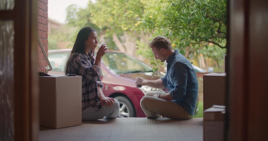 A man and woman take a break from moving boxes to set down and enjoy a small drink
