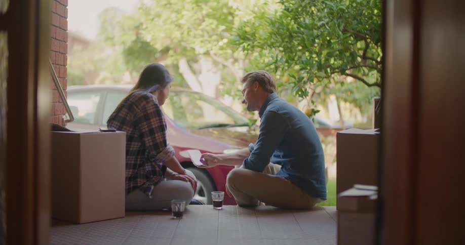 A man and woman take a break as they sit on the steps to a building and are surrounded by moving boxes