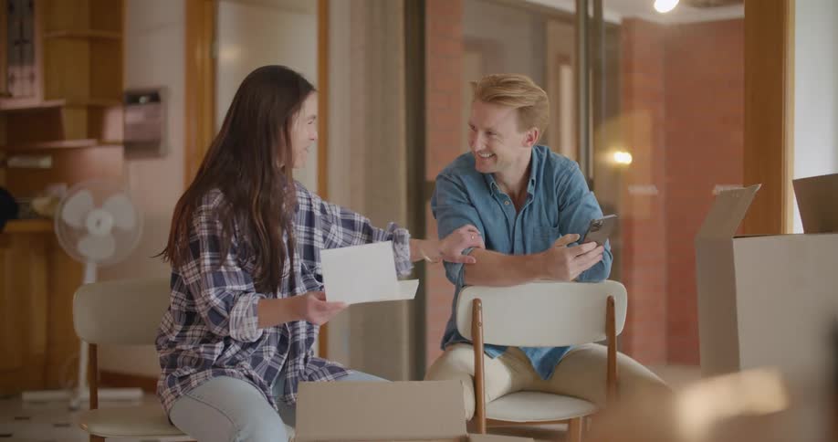 A man and woman smiling and talking while looking at a piece of paper indoors