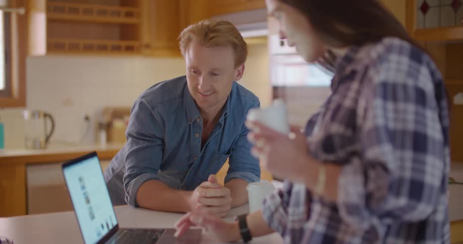 A woman holds a coffee cup and nods as she and her husband scroll on a laptop