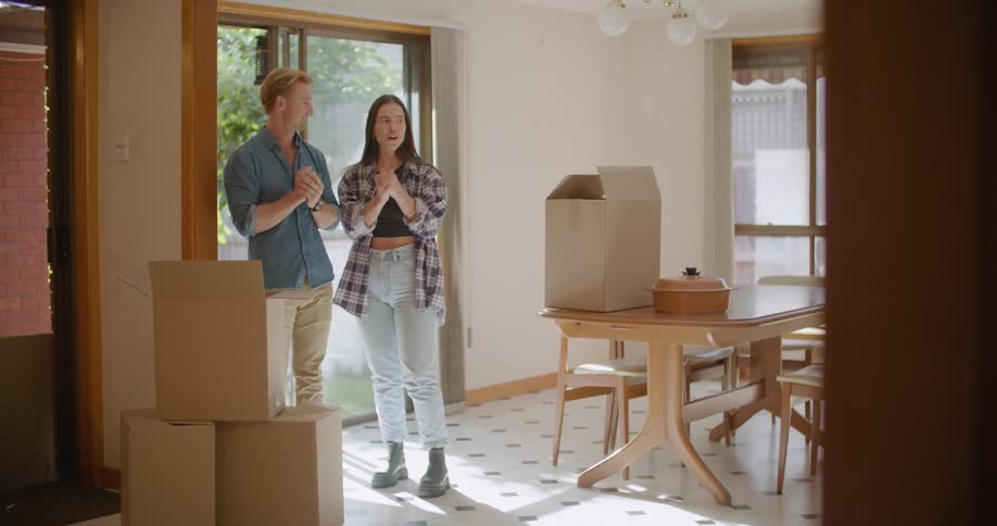 Blonde man with a blue shirt and woman in jeans and a plaid shirt stand next to the boxes and exchange opinions in the new house