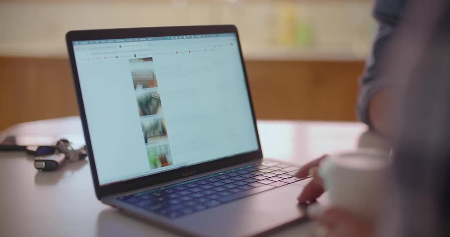 Woman browses website for new furniture on laptop in the the kithcen