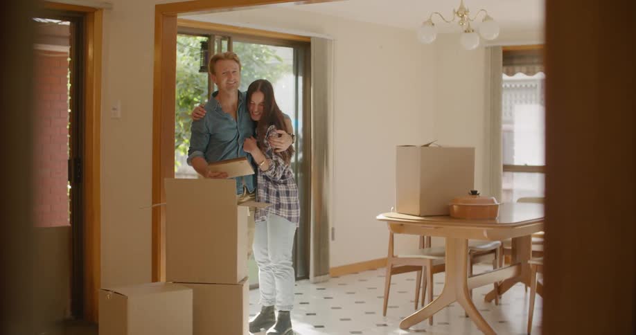 Young couple hugh each other while moving cardboard boxes into the house