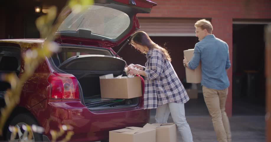A man and a woman taking boxes from a vehicle with a garage in the background