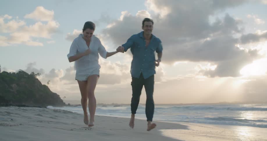 A man and woman holding hands while running barefoot on a sandy beach