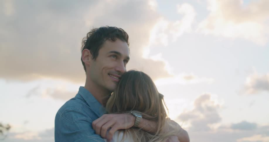 Young couple hugging on the beach next to the ocean at sunset