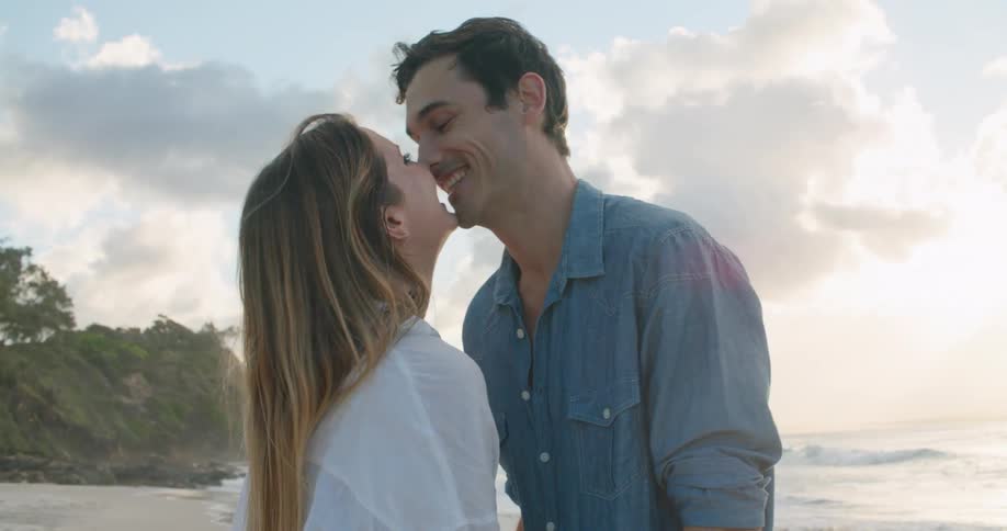 A man standing on the shore pulls his girlfriend towards him and laughs and they kiss