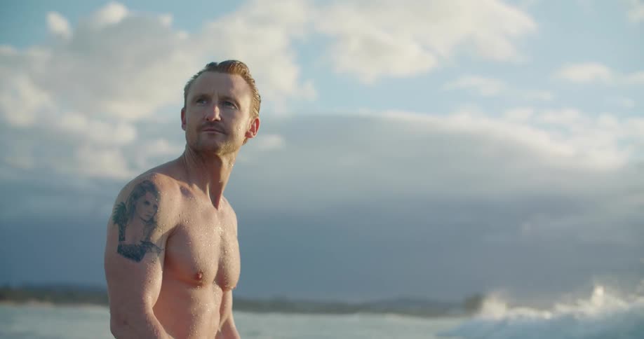 A shirtless man standing in ocean waves on a cloudy summer day
