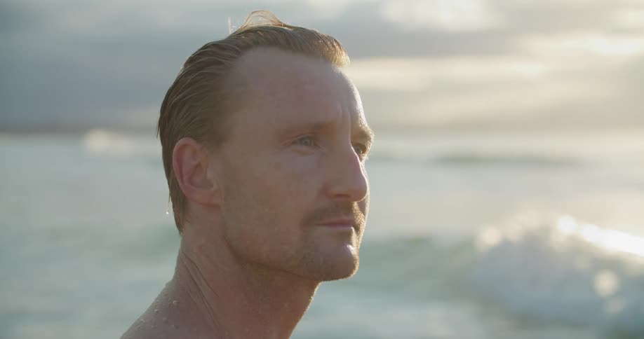 Man standing on the beach next to the ocean looks at the horizon at sunset