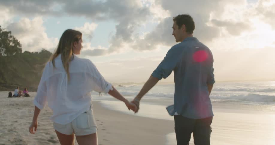 Husband and wife are walking on the beach together at dusk