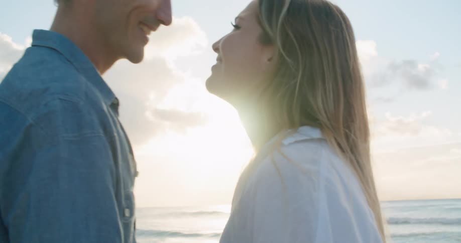 A man and a woman standing on a beach kissing with the sky and clouds in the background