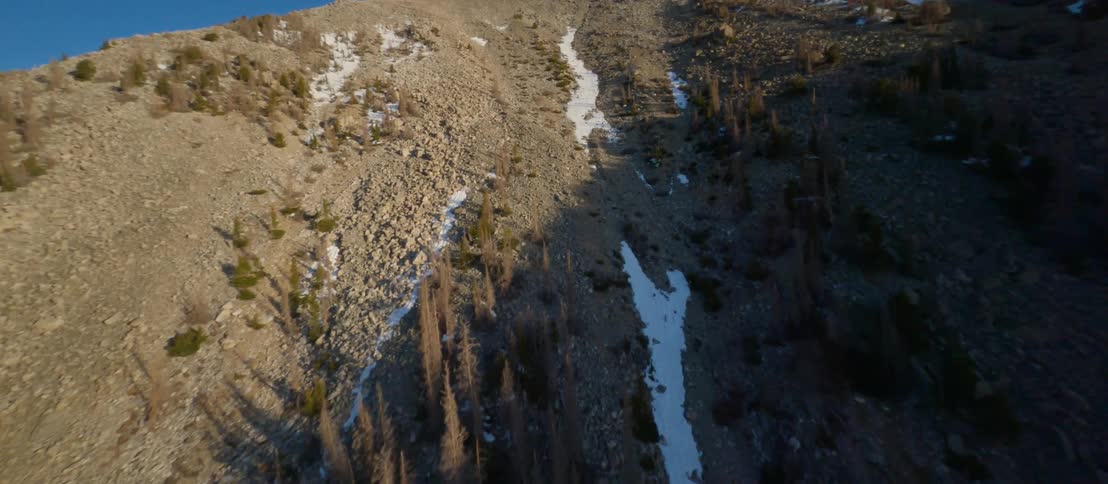 A mountain slope covered in gravel and sparse vegetation on a sunny day